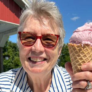 Jean in red glasses smiling holding an ice cream cone